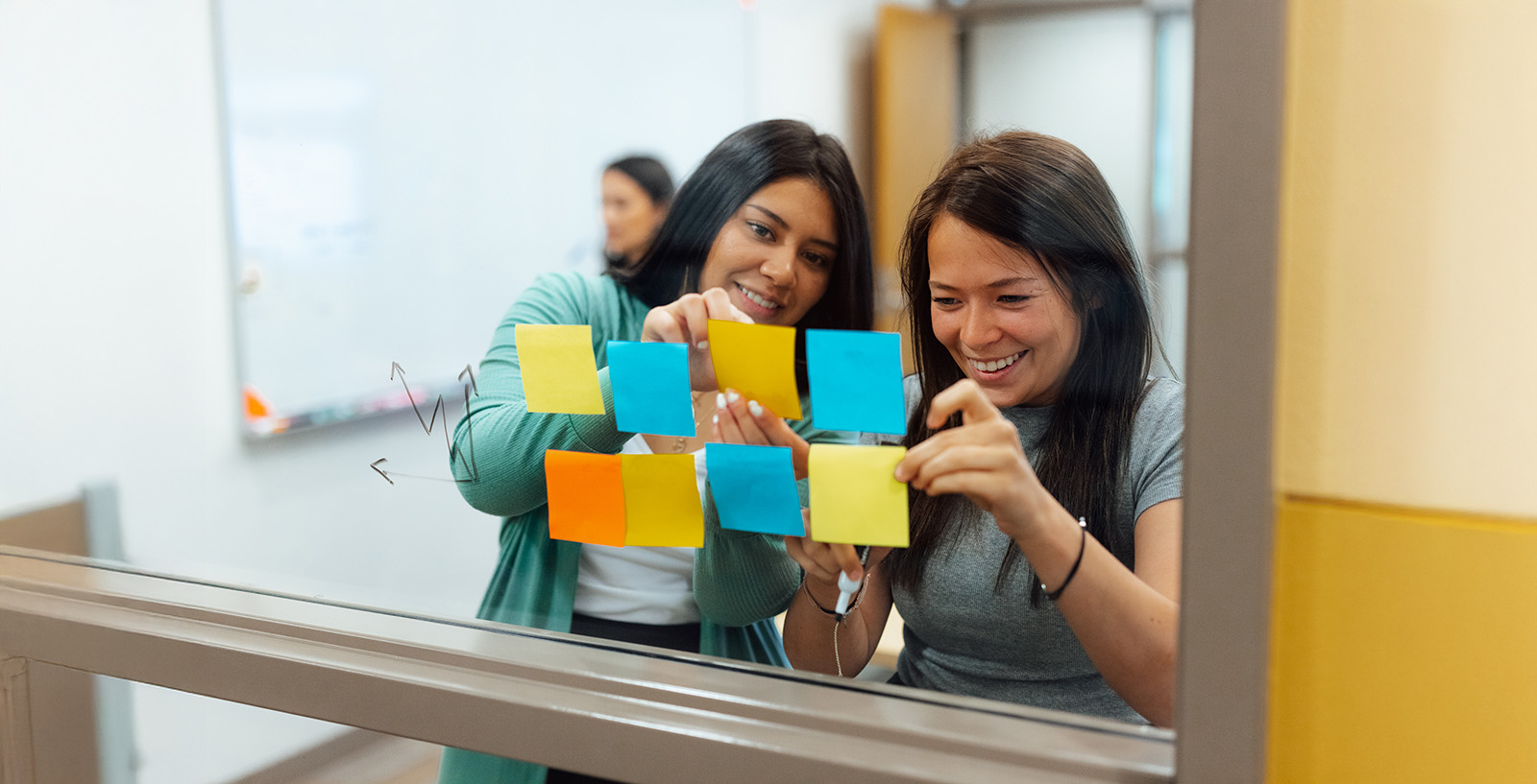 Students organizing ideas with sticky notes on a glass board during a collaborative session.