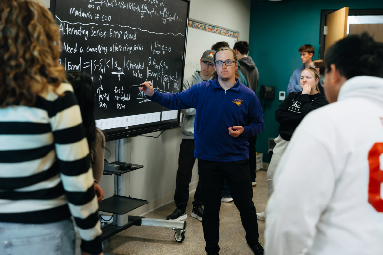 Instructor teaching a group of students using a digital board with mathematical concepts displayed.