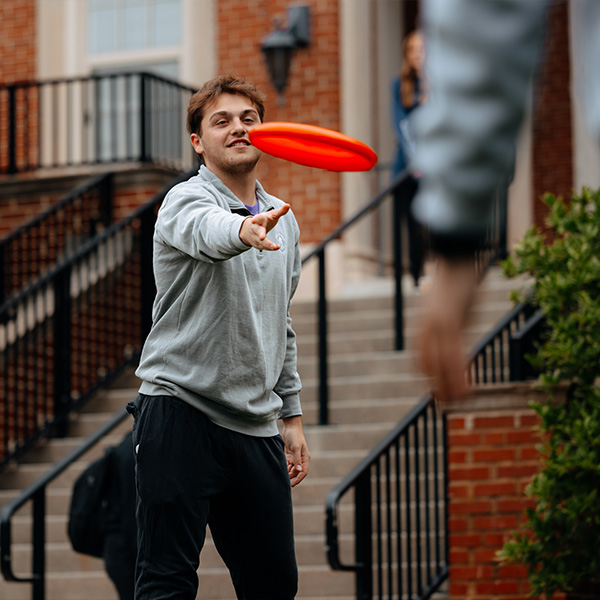 STEM business student playing frisbee on campus outside academic building.
